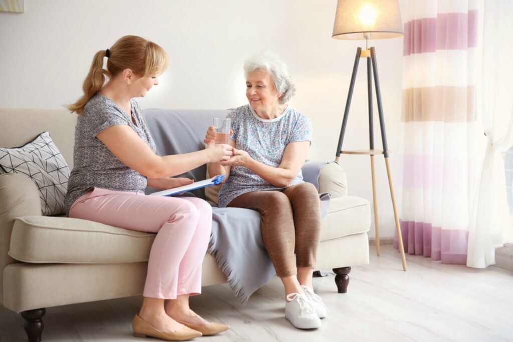 Caregiver giving glass of water to senior woman at home