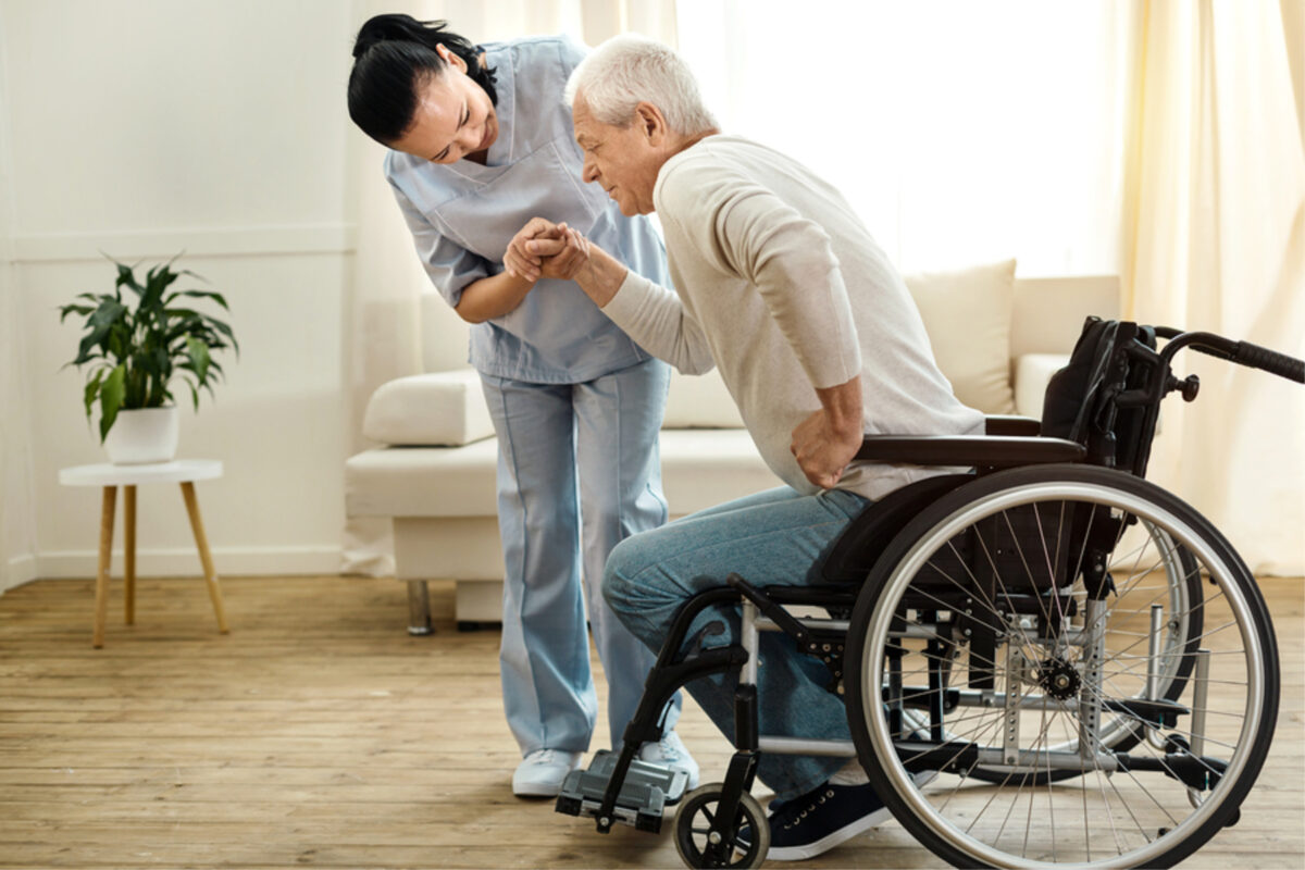 private nurse helping an elderly man stand up from the wheelchair