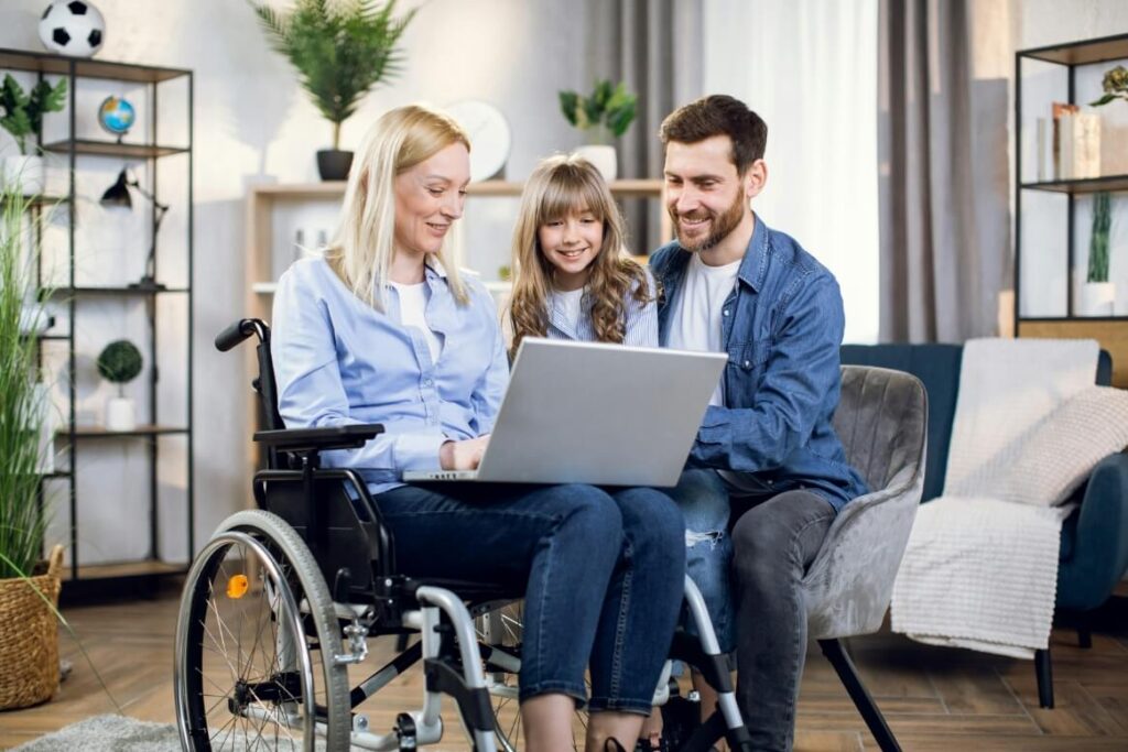 woman in a wheelchair using a laptop with her husband and child