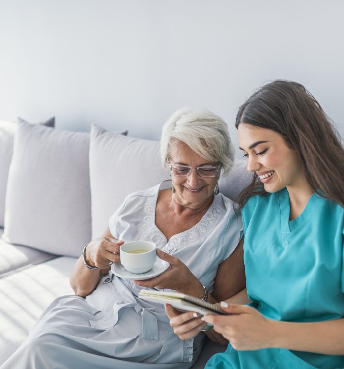 elderly woman and a home health assistant sitting on the couch while both are looking at the notebook