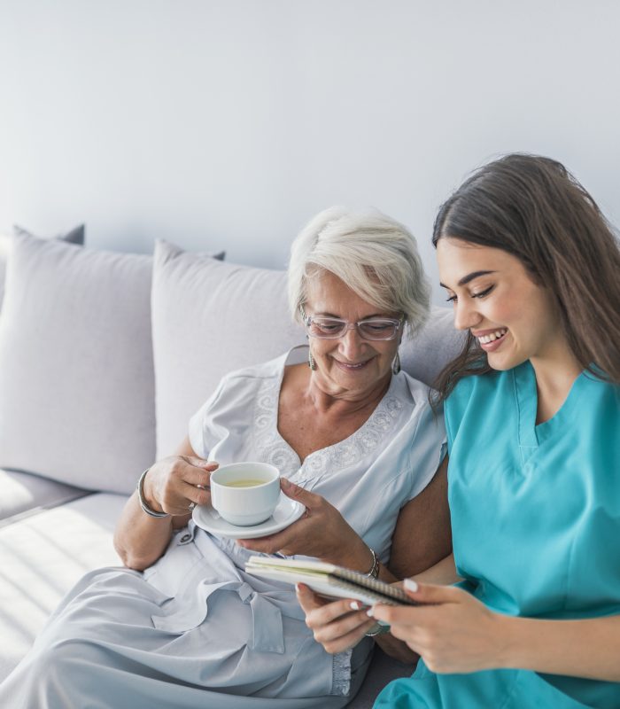 elderly woman and a home health assistant sitting on the couch while both are looking at the notebook