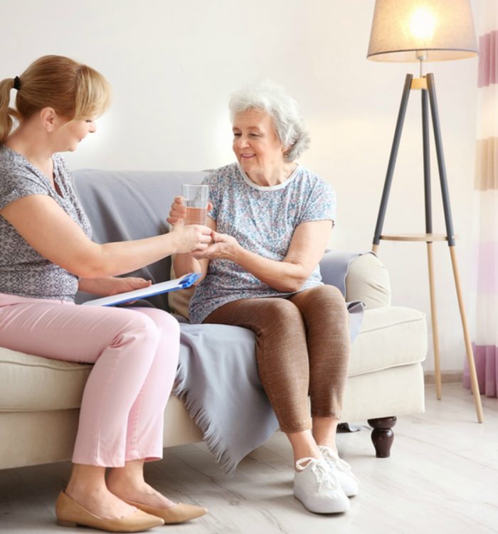 Caregiver giving glass of water to senior woman at home