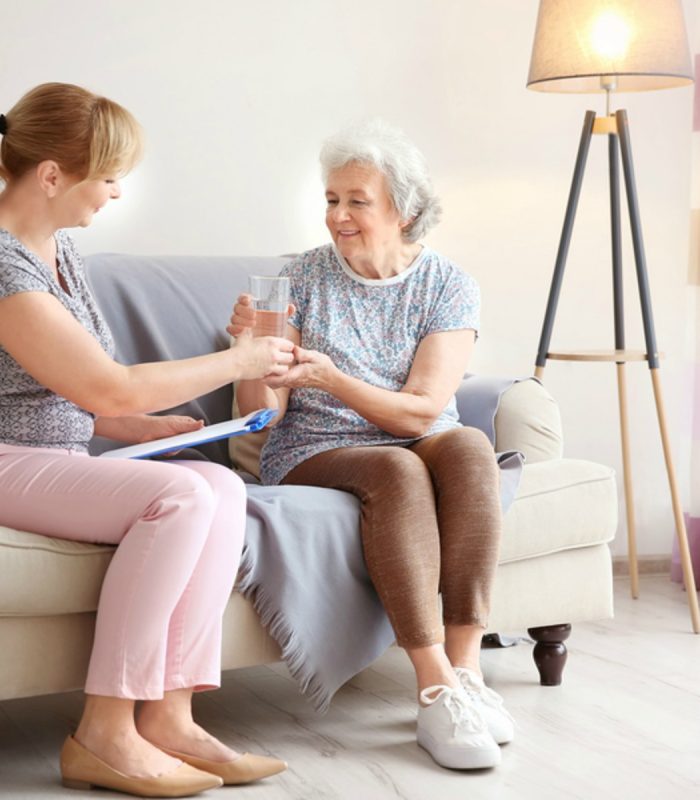 Caregiver giving glass of water to senior woman at home